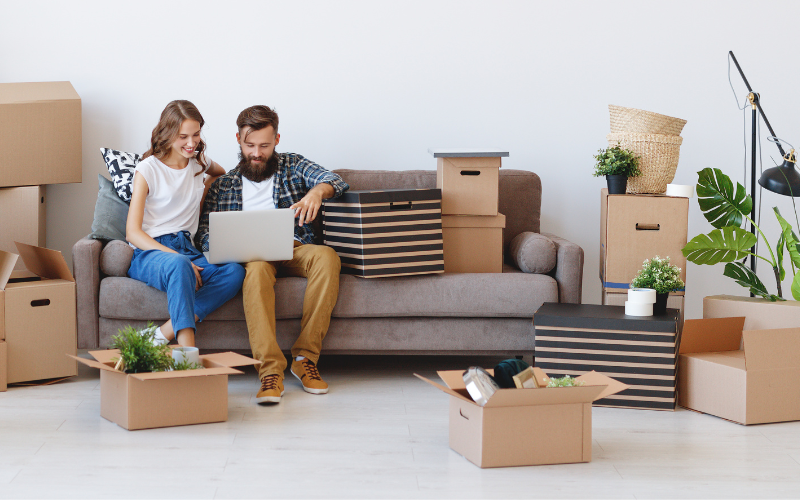 Couple surrounded by moving boxes looking at laptop monitor